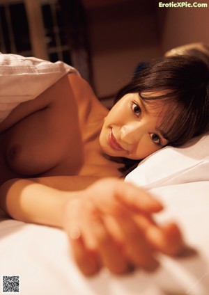 A naked asian woman laying on a bed.