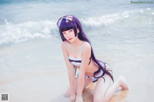A woman in a bikini standing on a rock by the ocean.