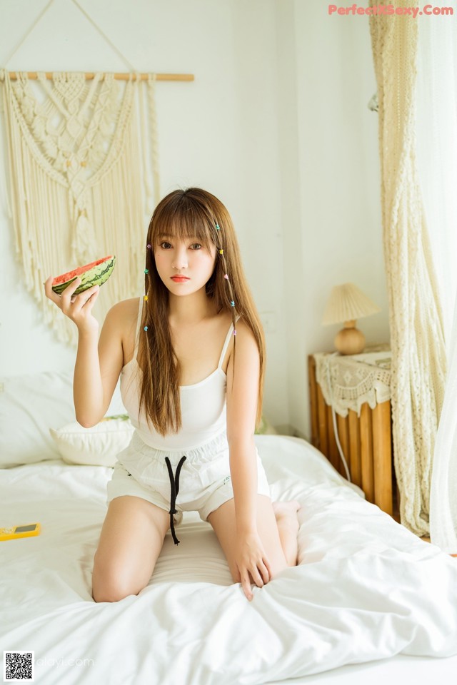 A woman sitting on a bed holding a slice of watermelon.