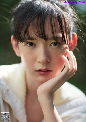 A woman leaning against a wall wearing a yellow sweater and white shorts.