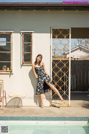 A woman in a blue floral dress leaning against a fence.