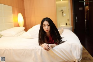 A woman in a red lingerie sitting on a bed.