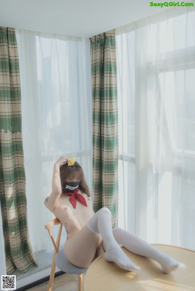 A naked woman sitting on a chair in front of a window.